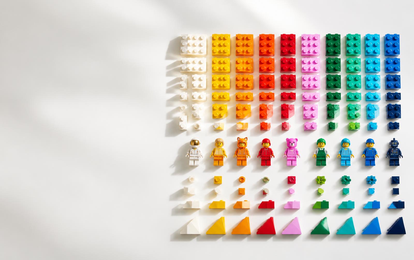 Peças de construção coloridas e minifiguras organizadas por cor sobre fundo branco